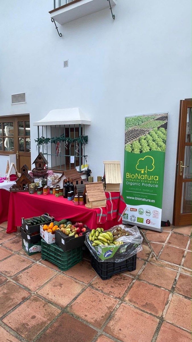 Mesa de exposición con fruta, verdura, tarros, botellas y casitas de madera.